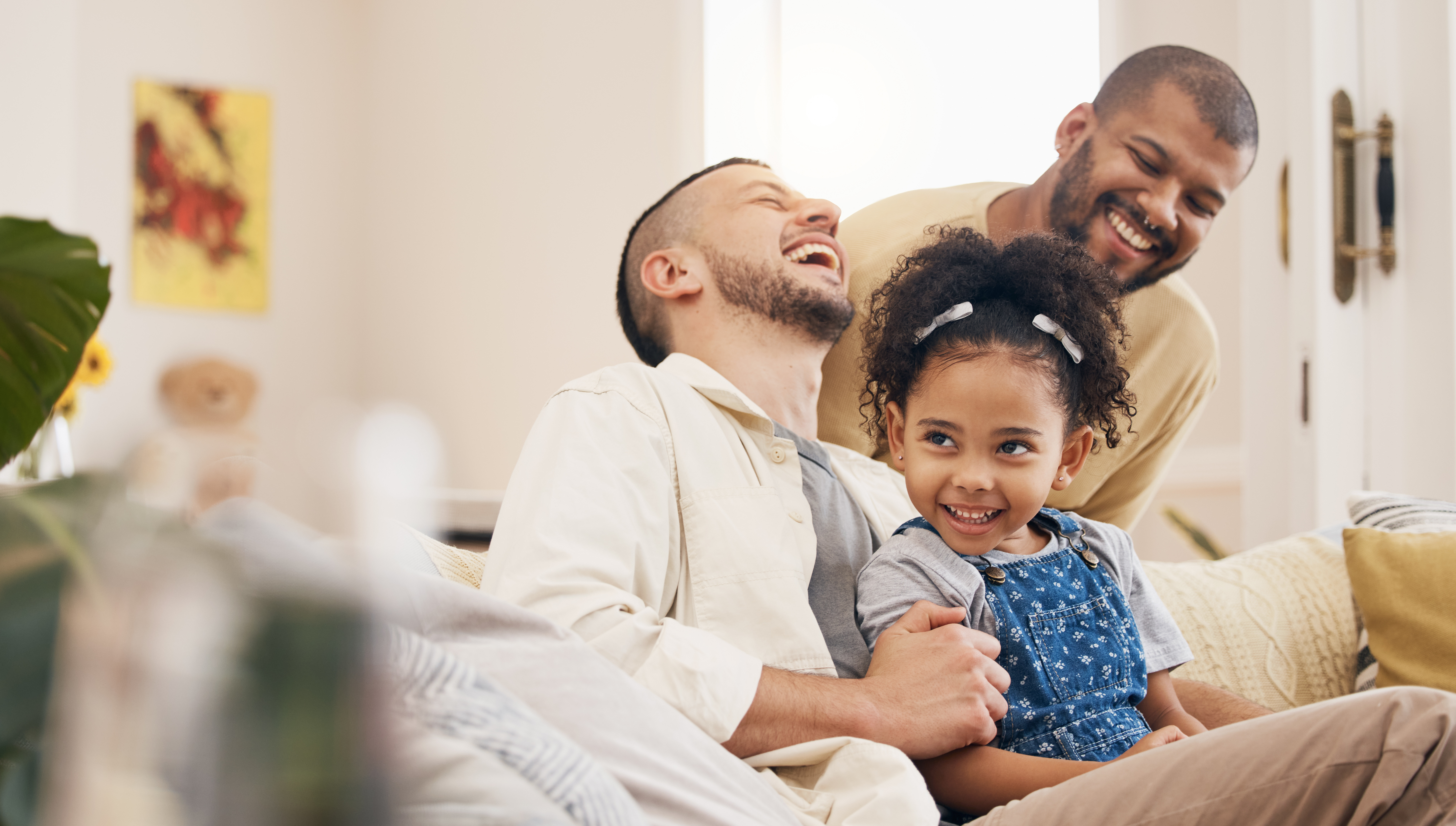Gay family, laughing and a child on a home sofa with love, care and funny joke in lounge. Lgbtq men, adoption and parents with foster girl kid together on a couch for happiness, bonding and to relax Gay family, laughing and a child on a home sofa with love, care and funny joke in lounge. Lgbtq men, adoption and parents with foster girl kid together on a couch for happiness, bonding and to relax.